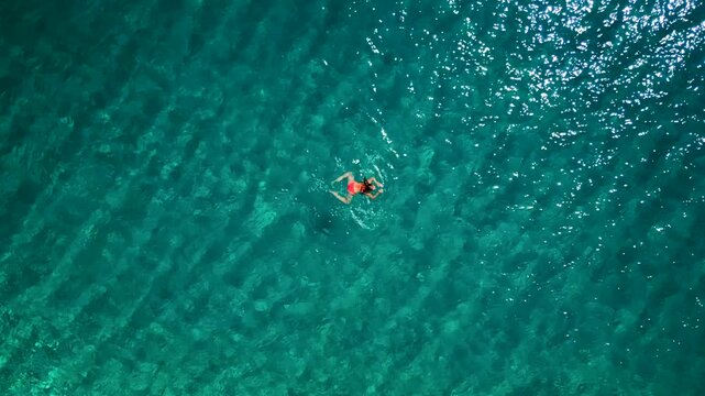 Woman in pink swimsuit swims in the clear sea, top down view