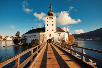Scenic view of historic castle on the water with wooden bridge leading to entrance, surrounded by nature and blue sky, showcasing architectural beauty