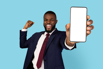 Online Profit. Overjoyed Black Businessman Holding Blank Smartphone And Celebrating Success, Cheerful African American Male In Suit Showing Mobile Phone With White Screen At Camera, Mockup