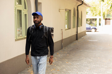African American courier delivers a hot meal order stopping at doorstep. Delivery man uses the...