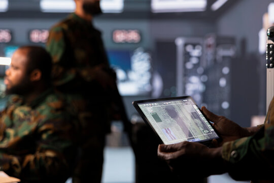 Military operator monitoring enemy aerial attacks using digital device. Army soldier in headquarters maintains air space superiority with radar on tablet during armed conflict, close up