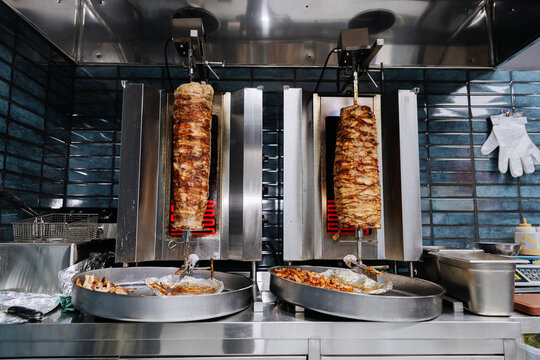 Two vertical shawarma grills cooking seasoned meat in stainless steel restaurant kitchen