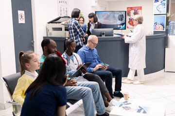 Female general practitioner with clipboard sits between elderly man and young black man in clinical...