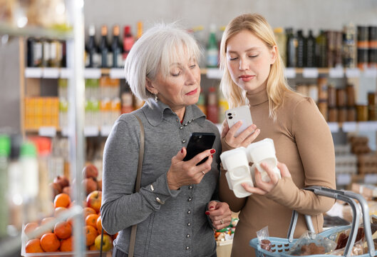Girl with senior female relative in store scan QR code on yogurt label. In mobile app, buyer receive information about yogurt. They check manufacturer data in registry database of national agency
