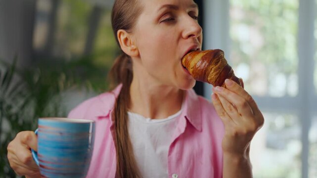 Woman enjoying fresh croissant and coffee for breakfast. Slow motion