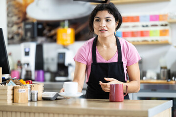 Young woman barista serving freshly brewed coffee in cup in cafe