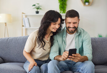 Couple family using smartphone together, browsing and reading social media feed at home. Young man...