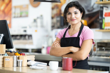 Polite young waitress in apron welcomes clients in casual urban cafe
