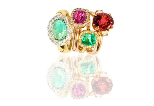 collection of elegant gold rings with large colorful gemstones, including emerald, ruby, and tourmaline. Luxury fine jewelry displayed on a reflective surface