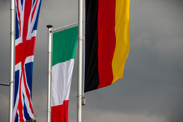 Flags of various countries, including the United Kingdom, Italy, Germany, and others, waving in the wind against a dramatic cloudy sky, symbolizing international unity and diversity