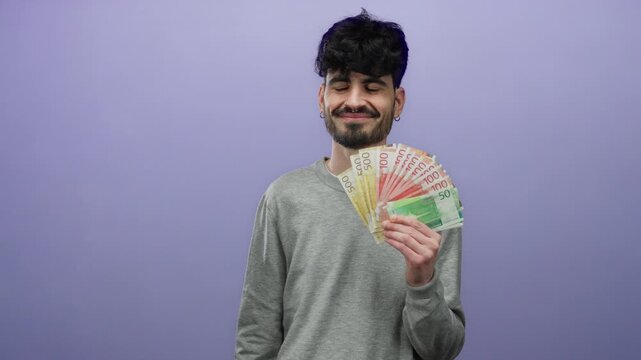 Young man holding norwegian banknotes against a purple background, showcasing krone currency in a casual setting with a confident expression