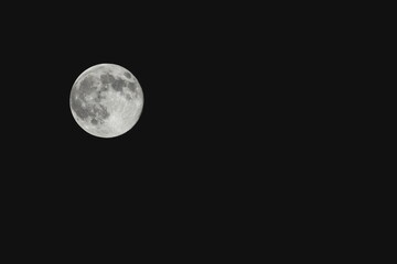 Close-up black and white photograph of the full moon against a dark night sky, showing detailed craters and surface texture.