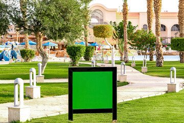 Blank green screen chroma key advertising commercial billboard banner at grass lawn on hotel territory,summer tropical resort.poster on street.template mock-up.