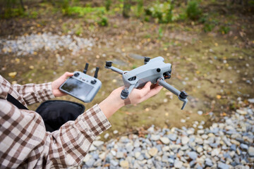 A person holds a sleek drone in one hand and a remote control in the other, ready to take off in a peaceful natural environment with soft lighting.