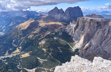 North-west view from upper station of Sass Pordoi cable car. Sassolungo or Langkofel Group, distinct twin-peaked massif directly beyond the Pordoi Terrace. Panorama with serpentine road.
