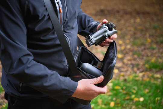 A photographer stands in a lush outdoor area, getting ready to shoot. He carefully handles his camera and bag, surrounded by colorful autumn foliage.