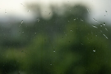 Raindrops on a window with a blurred view of green trees outside. A calm and melancholic atmosphere that evokes peace and introspection.
