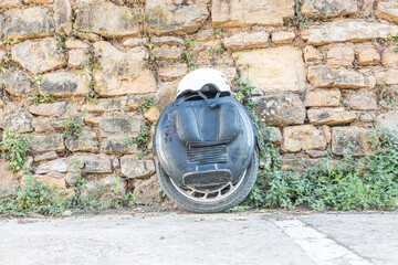 Black Electric unicycle and a white helmet leaning against a yellow stone wall