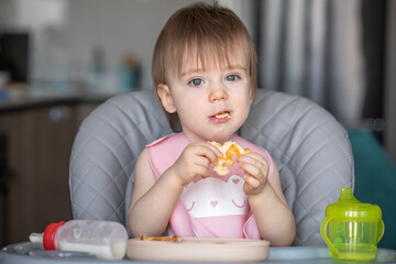 Infant girl eats deliciously while sitting at a childrens table