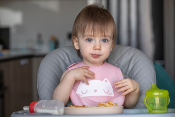 Infant girl eats deliciously while sitting at a childrens table