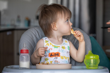 Infant girl eats deliciously while sitting at a childrens table