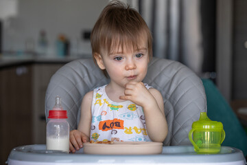 Infant girl eats deliciously while sitting at a childrens table