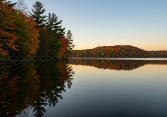 Obraz premium Beautiful autumn colors reflecting vividly on the calm surface of a massive freshwater lake, featuring glowing foliage under clear sunset skies ,reflection ,autumn ,sunlight