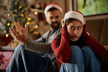 Displeased woman covering her ears while arguing with her boyfriend on Christmas day.