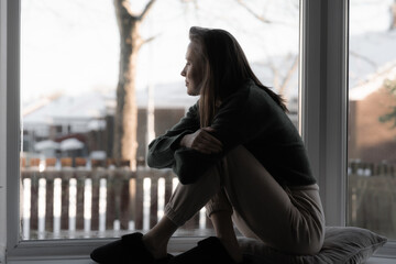 Thoughtful sad woman sitting on a windowsill. Mental health and seasonal disorder. Winter scenery...