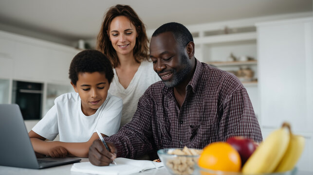 Warm family learning moment in a bright modern kitchen. A Black father helps his teenage son with homework at the kitchen table, while the red-haired mother stands nearby holding t - Powered by Adobe