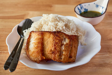 Delicious fried fish served with fluffy rice and flavorful sauce on a rustic wooden table