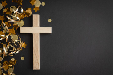 Wood cross and gold party streamers on a black background