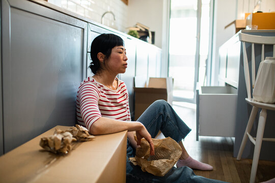 Adult woman overwhelmed unpacking boxes on kitchen floor