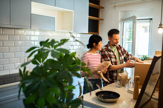 Adult couple unpacking kitchenware in new home kitchen, focused
