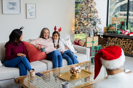 Diverse family sitting around coffee table in living room near Christmas tree sipping hot drinks
