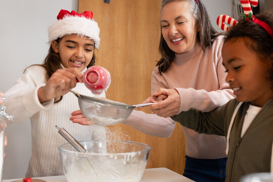 Diverse family preparing baking mixture in home kitchen using red measuring cup, sifter and bowl