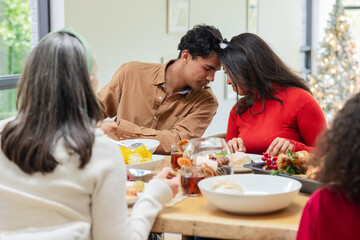 Diverse family sharing meal around wooden table at home with Christmas tree and bowls of corn