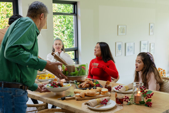 Family members passing salad bowl and sharing festive dishes around wooden dining table at home