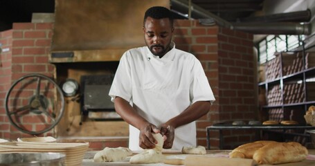 Baker wearing chef jacket shaping dough at bakery worktable, with brick oven gauge and metal racks