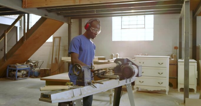 Mid adult male carpenter shaping spindle on lathe in woodshop, with goggles and earmuffs