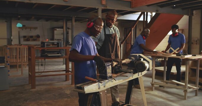 Operating wood lathe, mid-adult man wearing blue shirt turning wooden log in workshop, with chisels - Powered by Adobe