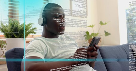 Scrolling phone, man in white T-shirt with over-ear headphones reading code overlay on blue sofa