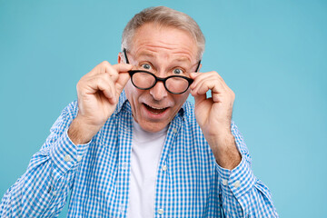 A mature man wearing glasses stares at the camera with a shocked expression. He appears amazed by...