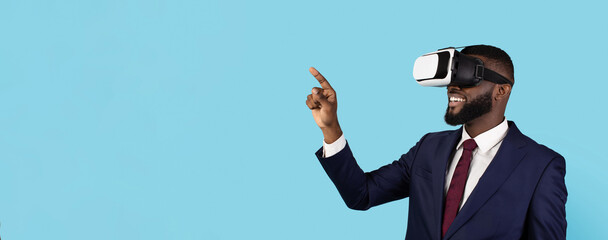 Modern Technologies For Business. Portrait Of Smiling Black Businessman Wearing VR Headset, Happy African American Male Entrepreneur Playing Video Game And Pointing Aside Over Blue Blackground