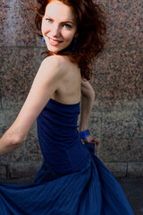 Energetic Woman in Blue Dress Dancing in Front of Urban Brick Wall
