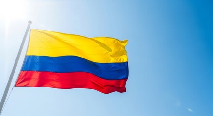 Naklejka premium Flag of Colombia waving proudly against a bright blue sky, symbolizing national pride and independence, with copy space.