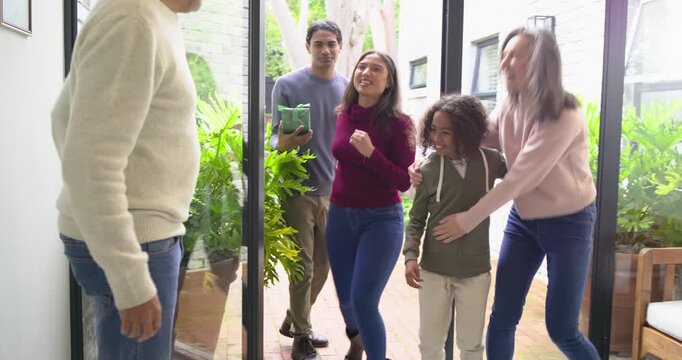 Mature couple opening glass double doors at entryway and welcoming arriving family with gift box