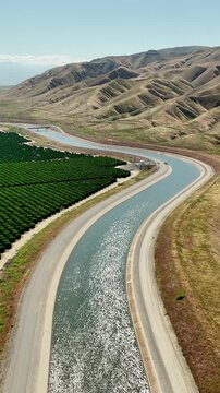Aerial of farms along an aqueduct running through California's Central Valley north of Los Angeles. Vertical video,