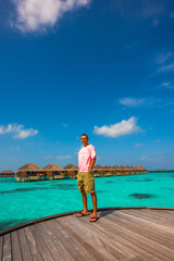Male tourist posing in front of bungalows. Tropical island beach landscape exotic shore coast. Tranquil closeup calm sea water waves. Summer vacation, holiday amazing nature. Relax paradise, Maldives.