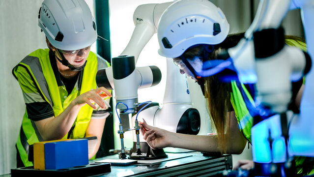 Two female robotics engineers in an R and D lab troubleshoot an artificial intelligence cobot. They are inspecting the robotic system hardware, sensors, and programming.